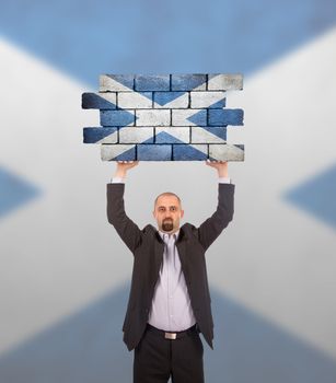 Businessman holding a large piece of a brick wall, flag of Scotland, isolated on national flag