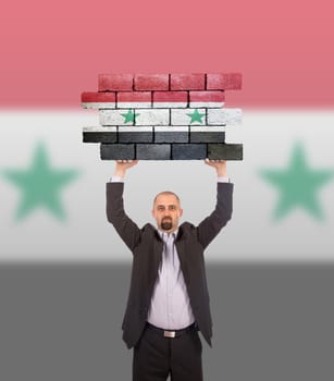 Businessman holding a large piece of a brick wall, flag of Syria, isolated on national flag