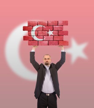 Businessman holding a large piece of a brick wall, flag of Turkey, isolated on national flag