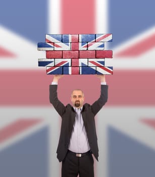 Businessman holding a large piece of a brick wall, flag of United Kingdom, isolated on national flag