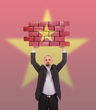 Businessman holding a large piece of a brick wall, flag of Vietnam, isolated on national flag