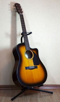 six-string acoustic guitar on a stand on light background