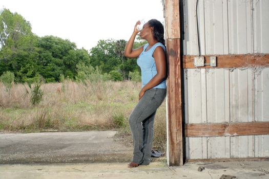 A lovely young black woman in casual wear cools off with a bottle of water.