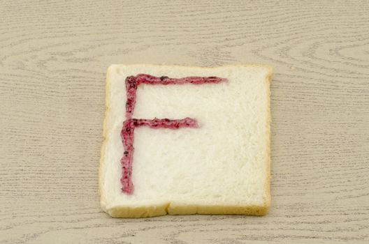 jam alphabet on sliced bread on wood background