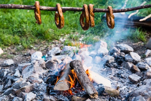 Gernan brezels being roasted on a long stick over a campfire in early evening twilight