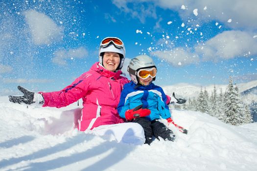 Skiing, winter, family - smiling boy in ski goggles and a helmet with his mother playing in snow in winter resort