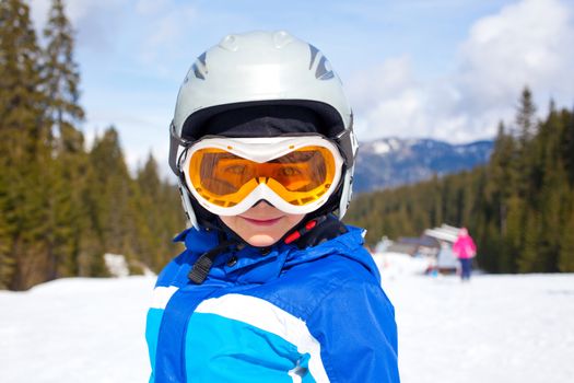 Portrait of little boy in helmet and ski goggles on a sunny day in the mountains. Active outdoor childhood concept