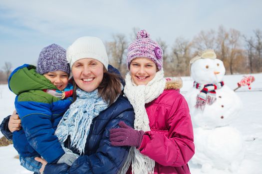 Happy mother with two kids building snowman outside in winter time