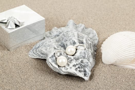 two pearl earrings and shells on sand background