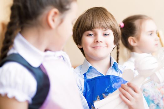 boy draws in the classroom with the other children, the children stand in a row in the table