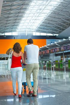 Back view of standing traveling couple with suitcases in airport