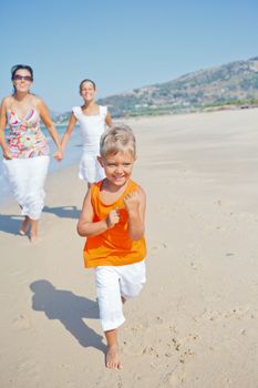 Adorable happy boy with sister and mother running on beach