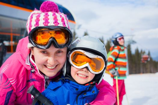 Portrait closeup of happy smiling boy in ski goggles and a helmet with his mother