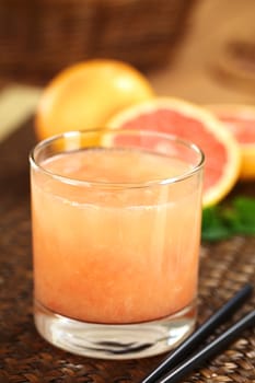 Freshly squeezed juice of the pink-fleshed grapefruit with black drinking straws on the side and grapefruits in the back (Selective Focus, Focus on the front rim of the glass)