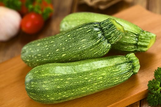 Raw zucchini on wooden board with other ingredients in the back (Selective Focus, Focus on the tip of the two zucchinis in the front)