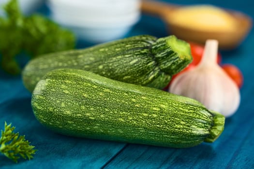 Raw zucchini on blue wood with other ingredients in the back (Selective Focus, Focus on the front of the first zucchini)