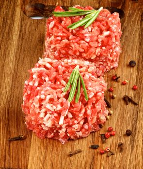 Two Fresh Raw Beef Burgers with Rosemary and Pepper Corns closeup on Wooden Cutting Board