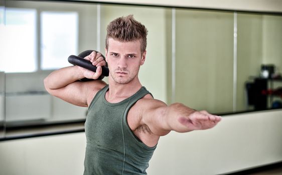 Attractive young man exercising with kettlebell, working out in gym