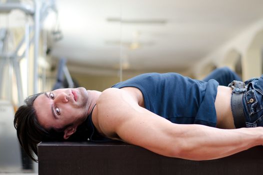 Handsome, sexy young man laying on his back, looking to a side, indoors in a gym