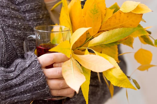 Female hand holding a glass of tea and autumn leaves