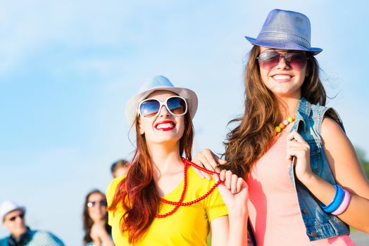 Two young girlfriends having fun on the background of blue sky and friends