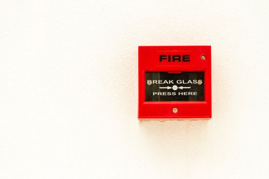 Red fire alarm switch on white concreat wall.