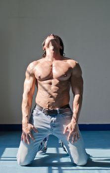 Handsome young muscle man shirtless kneeling on the floor, holding head up, wearing jeans