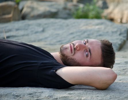 Handsome young man lying on his back on a rock, looking in camera, outdoors