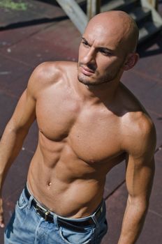 Attractive bald young man shirtless in jeans outdoors, serious expression, seen from above