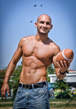 Fit young man naked with football in his hand, outdoors smiling