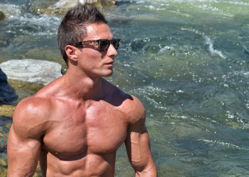Handsome young muscle man naked outdoors with water behind him, large copy-space