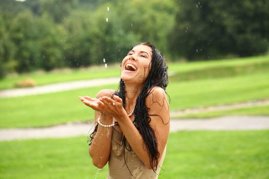 Young sexy brunette woman outdoor in a garden playing with water and rain with wet shirt