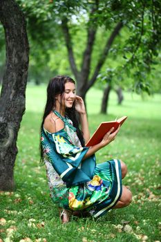 Portrait of beautiful young blonde girl reading a book in the park