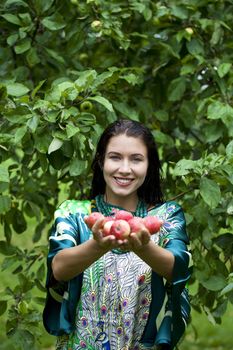 Young attractive woman holding apples, against green of summer park.