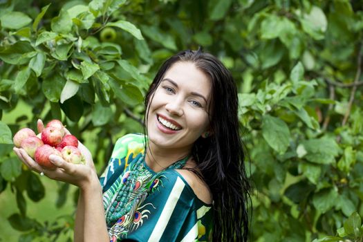 Young attractive woman holding apples, against green of summer park.