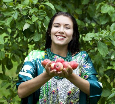 Young attractive woman holding apples, against green of summer park.