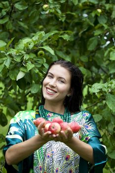 Young attractive woman holding apples, against green of summer park.