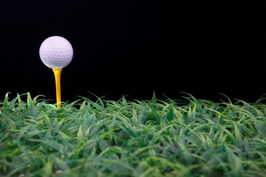 golf ball on yellow tee with green grass isolated black