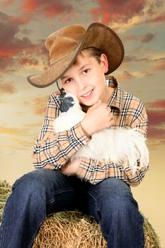 A country farm boy sitting on a lucerne bale and holding a bantam chicken at sunset