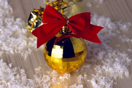 Golden ball with a red bow lying in the snow and beads