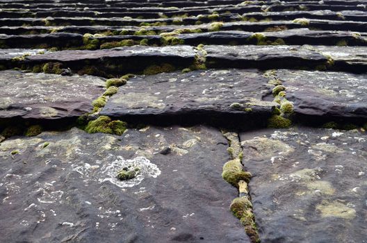 Close up view of a Medieval roof covered with large heavy slate roof tiles weathered with moss.