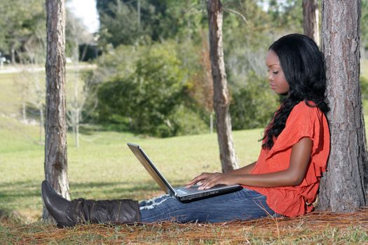 An extraordinarily beautiful young woman dressed in casual wear, works on her laptop computer outdoors.