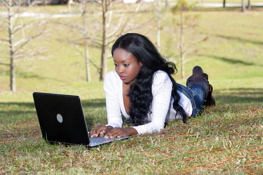 An extraordinarily beautiful young woman dressed in casual wear, works on her laptop computer outdoors.