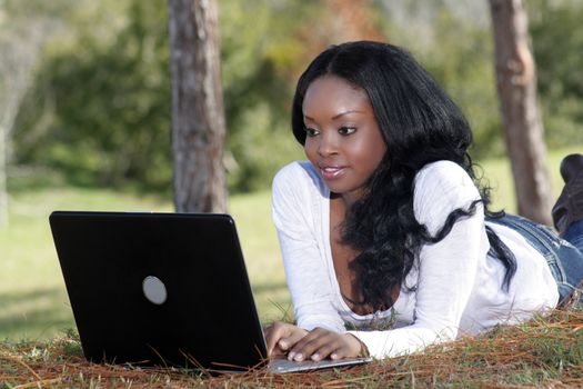 An extraordinarily beautiful young woman with a captivating smile, dressed in casual wear, works on her laptop computer outdoors.