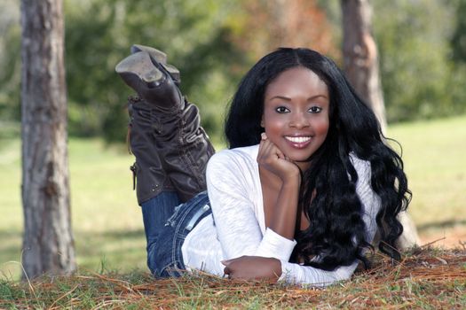 An extraordinarily beautiful young woman with a captivating smile, dressed in casual wear, lying in the grass outdoors.