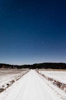 Long snowy road and clear starry sky in moon light