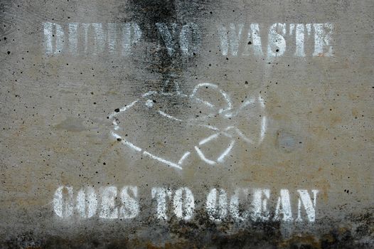 Weathered 'dump no waste goes to ocean' warning sign on concrete