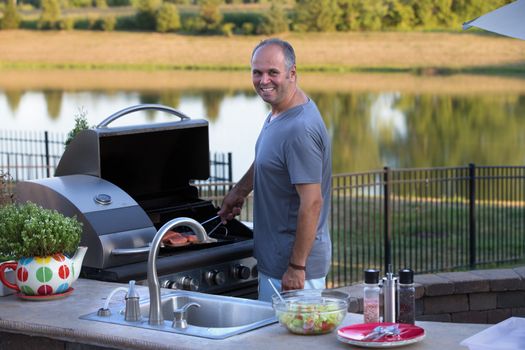 Middle age man cooking salmons at the outside kitchen barbecue