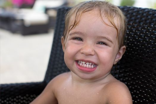 Little girl came out from water sitting on a beach chair with her wet hair, smiling large with her 18 teeth