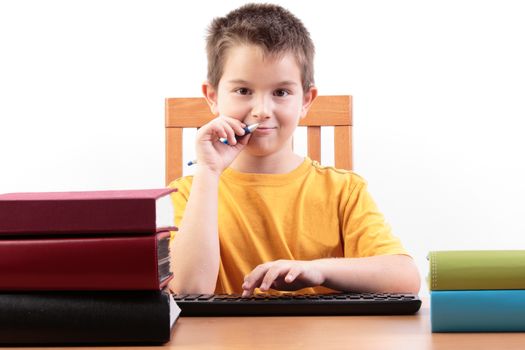 Young boy in his yellow T shirt looking at camera betwwen books and pointing his pen